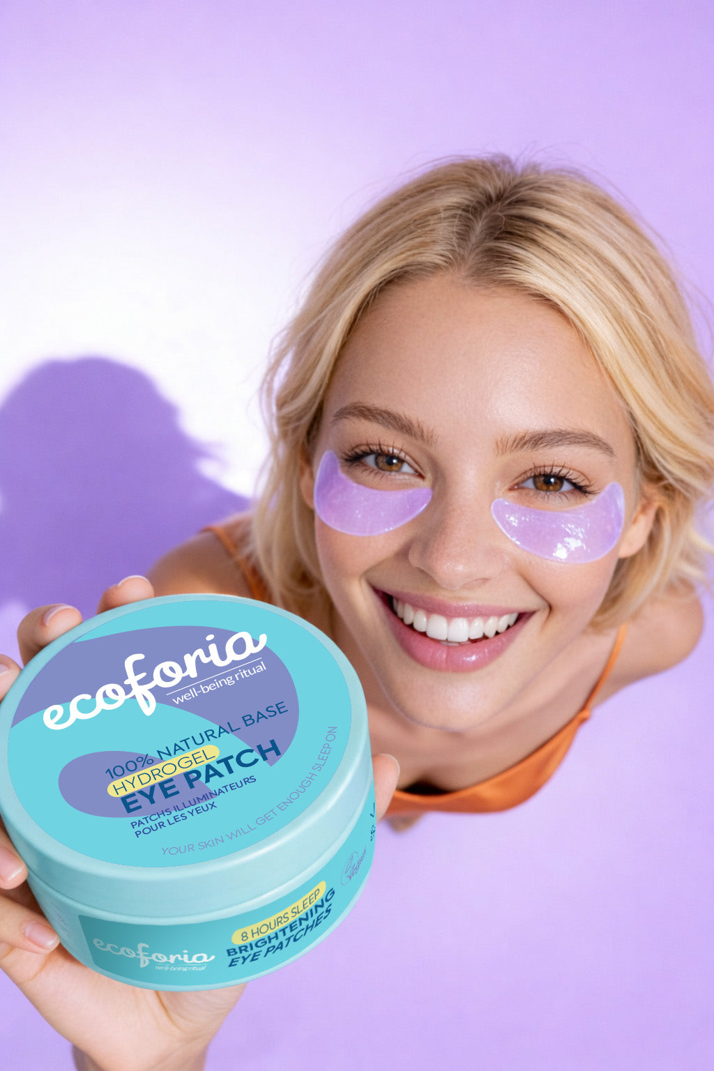 Woman wearing eye patches holding an ecoforia eye patch container against a purple background